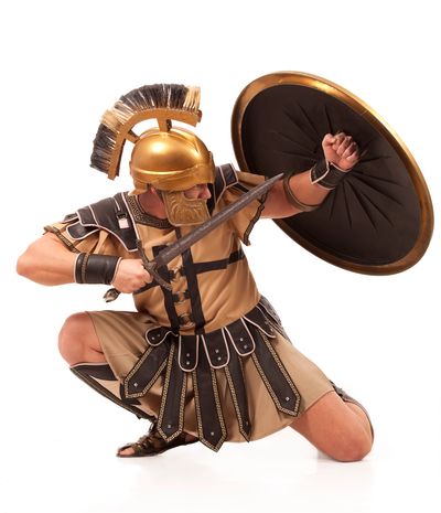 A warrior in ancient Greek armor crouching with a sword and shield.