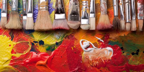 Variety of paintbrushes above vibrant mixed paints on a palette.
