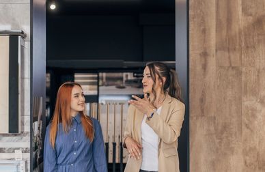 Two women talking and smiling in a modern bathroom showroom.