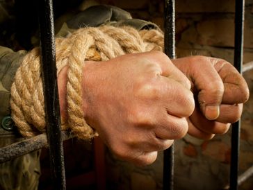 Hands tied with rope behind prison bars.
