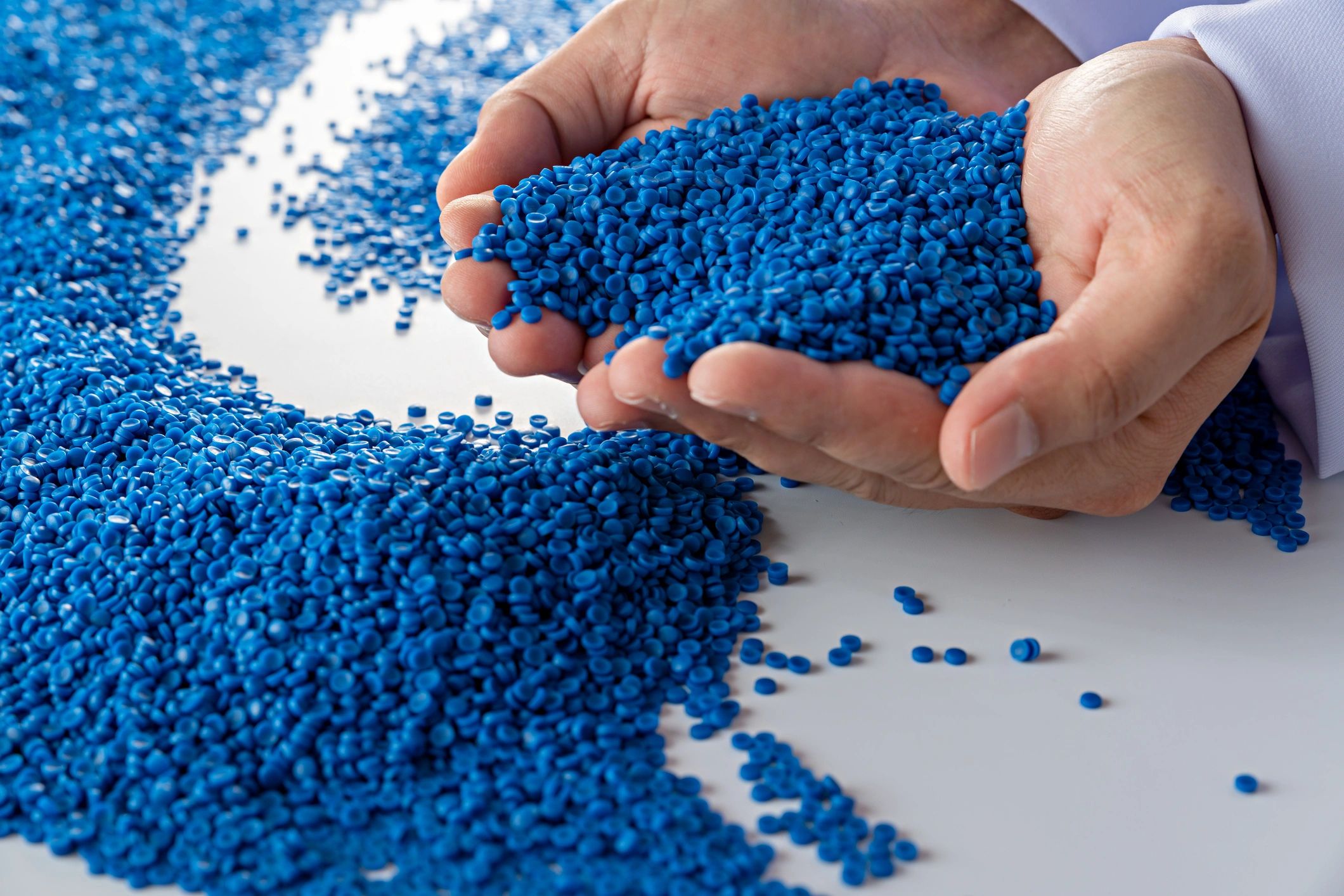 Hands holding small blue plastic pellets used in manufacturing.