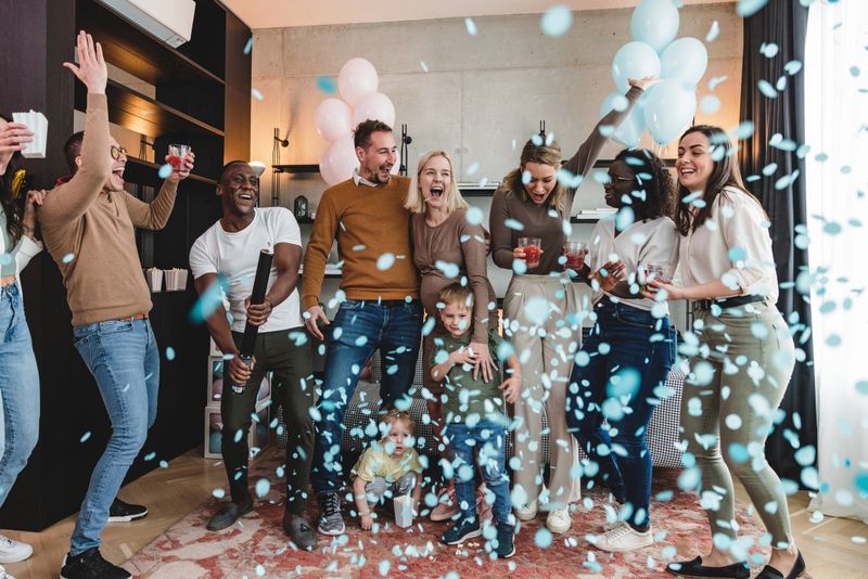Happy group of gender reveal party guests popping the confetti cannon to reveal the gender of the baby. The expectant couple finally found out they are having a baby boy. They are surrounded by their closest friends and look happy. The confetti is flying everywhere. A moment to remember.