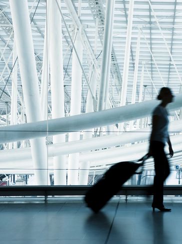 Silhouette of a person walking with a suitcase in a modern airport terminal.