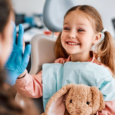 Smiling girl at dentist giving a high-five while holding a stuffed bunny.