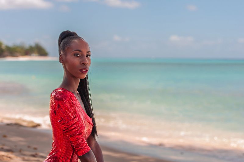 Portrait of Beautiful Caribbean Adult Teen in Barbados. Wearing Red Bikini and Sitting on a tropical beach. Caribbean Sea in Background. Black. Portrait.