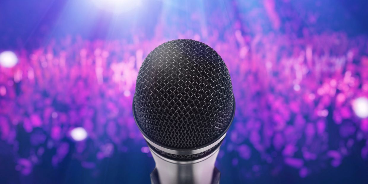 Close-up of a microphone with a vibrant purple crowd background.