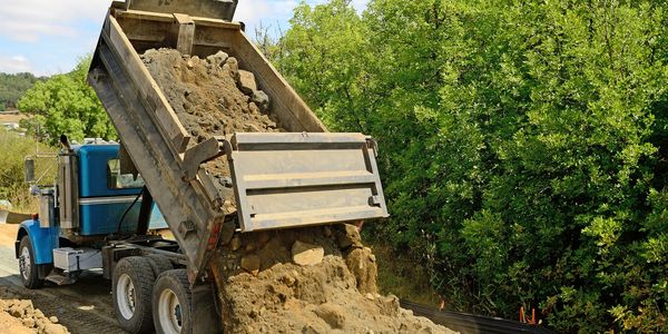 Blue dump truck dumping fill dirt at dump site in wooded area in Columbus Ohio
