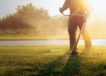 Person using a string trimmer to cut grass in sunlight.