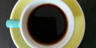 Top view of a coffee cup with black coffee on a yellow saucer.
