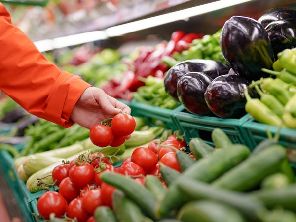 Person in orange sleeve picking fresh tomatoes at a grocery store.