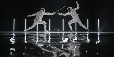 Two fencers engaged in a duel with reflections below.