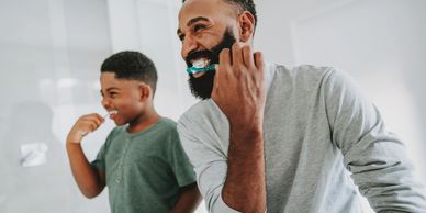 Father and son happily brushing their teeth together in the bathroom.
