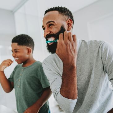 Father and son brushing teeth together.