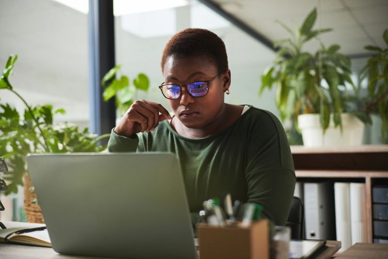 Thinking, research and business woman reading, article review and editing or news analysis in office. Focus, glasses reflection and African person, editor or journalist for online report on computer