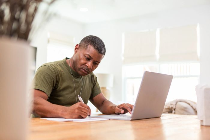 Man focused on writing notes while using a laptop at a wooden table for career advancement in HR training programs
