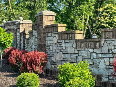 Stone and brick garden wall with red and green shrubs under bright sunlight.