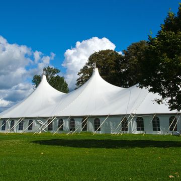 Team setting up a large frame tent on a grassy field for an outdoor wedding, event rentals, tent 