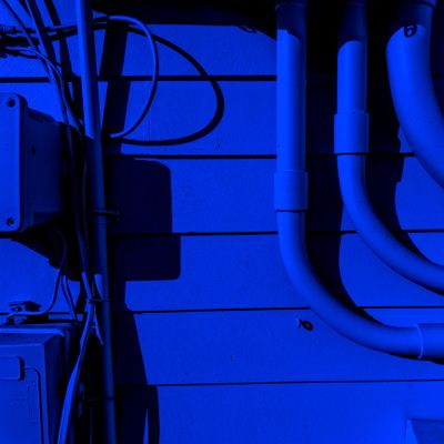 Blue-lit wall with pipes and electrical wiring casting shadows.