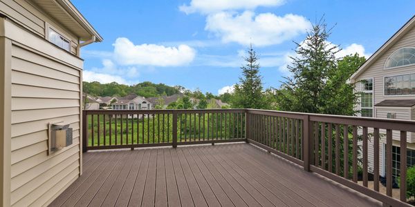 Spacious wooden balcony with brown railings overlooking green trees and neighboring houses.