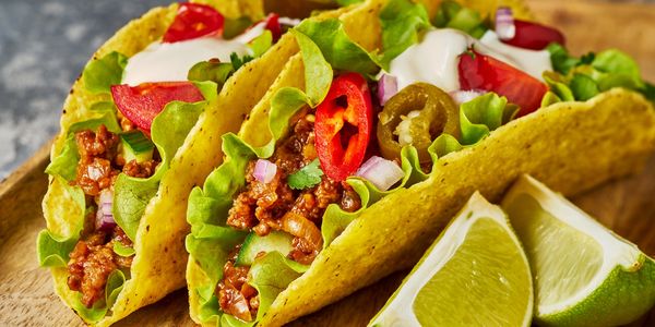 Two tacos filled with lettuce, ground meat, tomatoes, jalapeños, and a side of lime wedges.