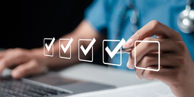 Hand marking checkboxes with a pen near a laptop.