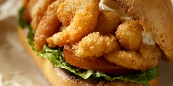 Close-up of a crispy fried shrimp po' boy sandwich with lettuce and tomato.