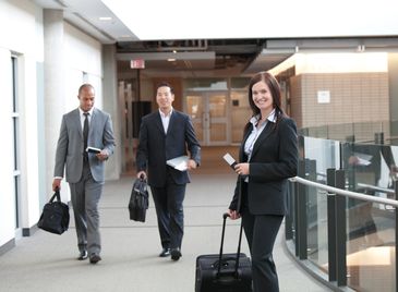 Business professionals walking in an airport corridor with luggage and briefcases.