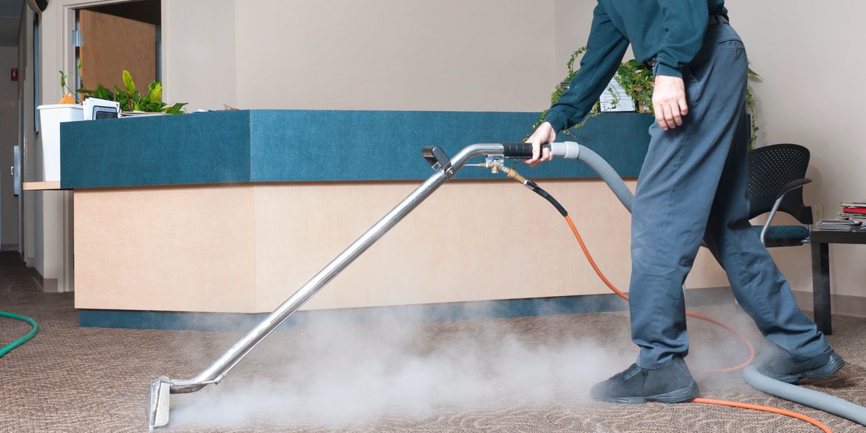 Person cleaning carpet with steam cleaner in office setting.