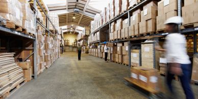Busy warehouse with shelves full of boxes and workers moving packages.