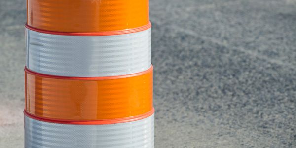 Close-up of an orange and white traffic barrel on a gray asphalt road.