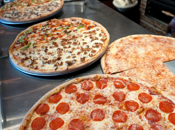 Four large pizzas with various toppings on a metal counter.