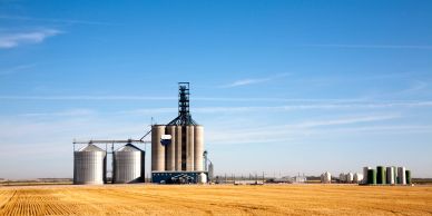 Grain storage silos beside a harvested prairie field under a clear blue sky.