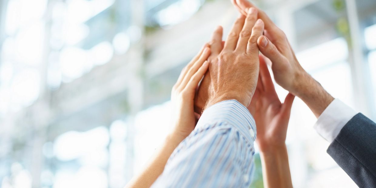 Multiple hands coming together for a high-five in a bright, professional setting.