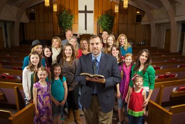 A pastor with a group of diverse children and adults inside a church.