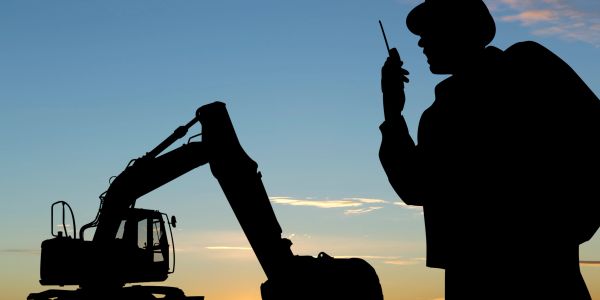 Silhouette of a construction worker with an excavator at sunset.