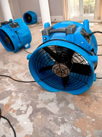 Blue industrial fans on a damaged floor in a room.