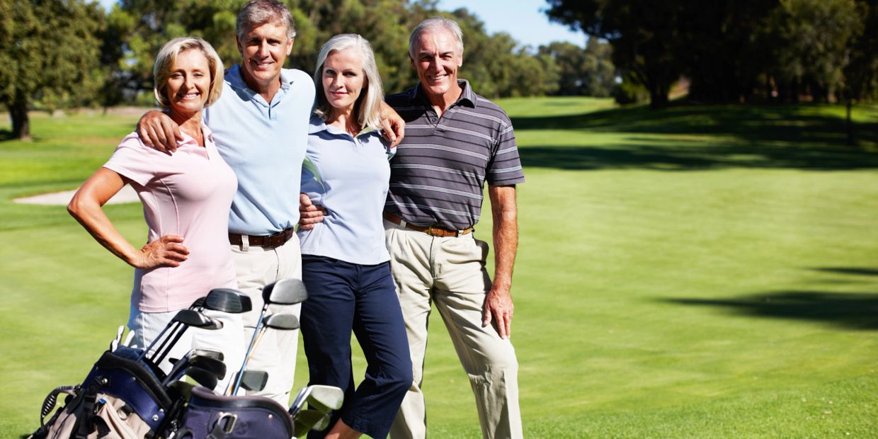 Four adults posing with golf clubs on a sunny golf course.