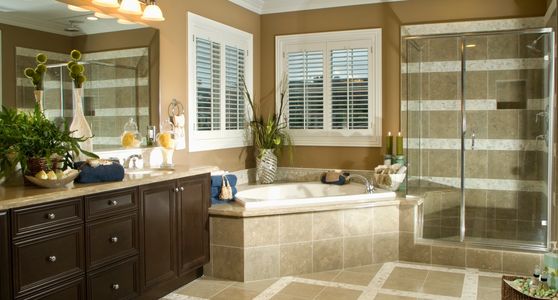 Bright bathroom with glass shower and large bathtub under shuttered windows.