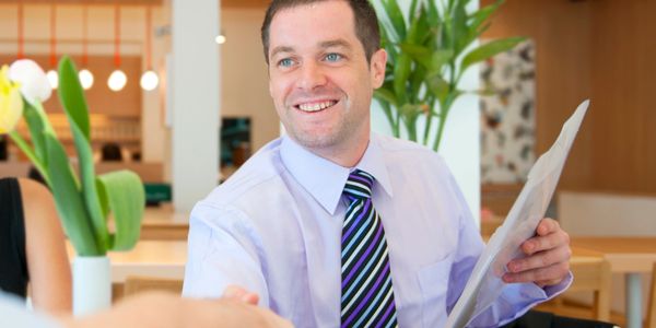 A man in a shirt and tie smiling while shaking hands and holding a document.