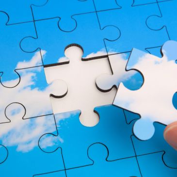Hand placing the last puzzle piece of a blue sky with clouds.