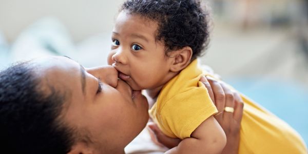 A mother lovingly kisses her baby who wears a yellow shirt.