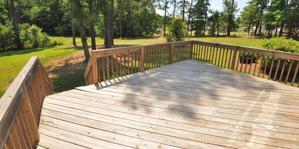 Empty wooden deck with railing overlooking a green yard.