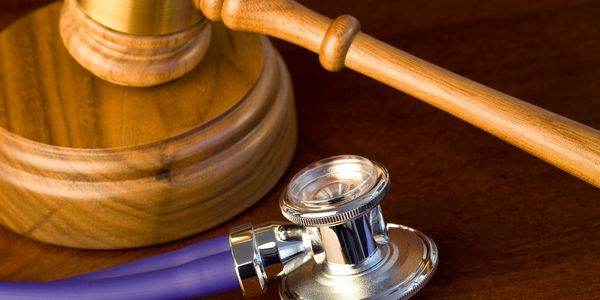 A wooden judge's gavel and a purple stethoscope on a wooden surface.