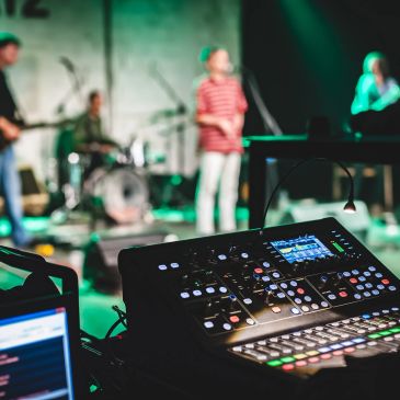 Sound mixing console in front of a band performing on stage.