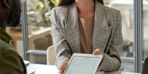 A woman in glasses shows a document on a tablet to a man with an arm sling.