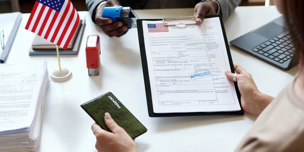 Person holding an approved U.S. visa application form and passport at a desk with an American flag.