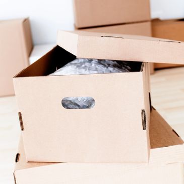 Open cardboard box filled with packing material and sealed boxes around.