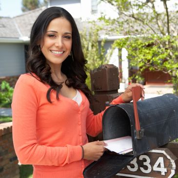 Woman smiling while checking mailbox outdoors.