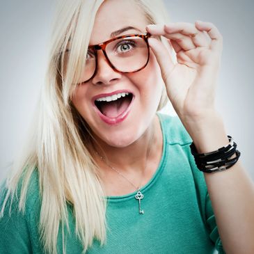 Excited woman with glasses smiling widely, wearing a green top.
