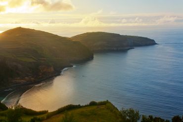 Sunset over a peaceful coastal bay with hills and calm sea.